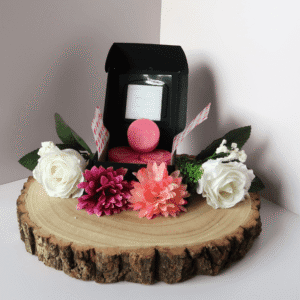 Baie Rose Wax Melt inside an open black box, surrounded by flowers, all sitting on top of a wooden board.