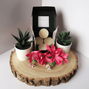 Elysian Elixir Wax Melt inside an open black box, surrounded by flowers and plants, all sitting on top of a wooden board.
