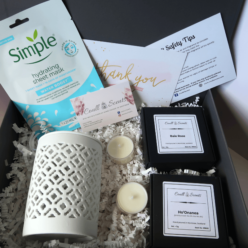 Pampering Wax Melt Gift Set showing Cut Out Wax Melt Burner, facial mask, 2 boxes of Wax Melts and 2 tealights, sitting on shredded paper in a grey box.