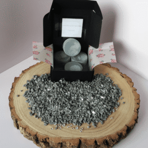 Pomegranate Eclipse Wax Melt inside an open black box, surrounded by grey pebbles and diamantes, all sitting on top of a wooden board.