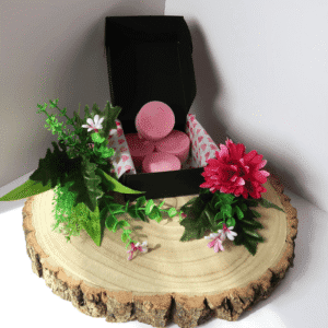 Sicilian Spring Wax Melt inside an open black box, surrounded by flowers, all sitting on top of a wooden board.