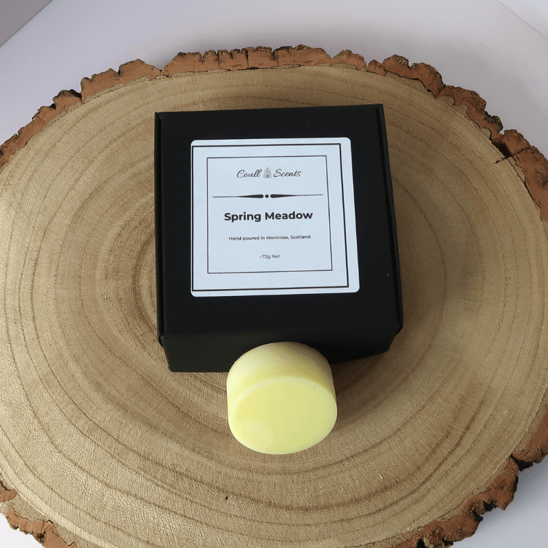 Spring Meadow Wax Melt outside its black box, sitting on top of a wooden board.