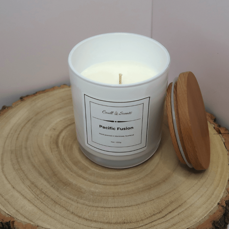 Pacific Fusion Candle in white container with wooden lid off and leaning against the container, sitting on top of a wooden board.