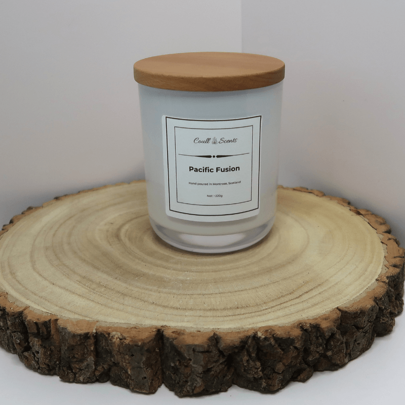Pacific Fusion Candle in white container with wooden lid on, sitting on top of a wooden board.